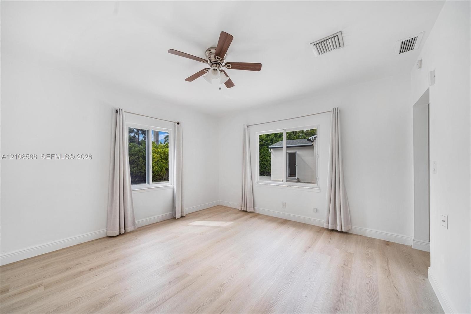 Bright room featuring wood-finish flooring, dual windows with sliding panes, and a ceiling-mounted fan with integrated lighting