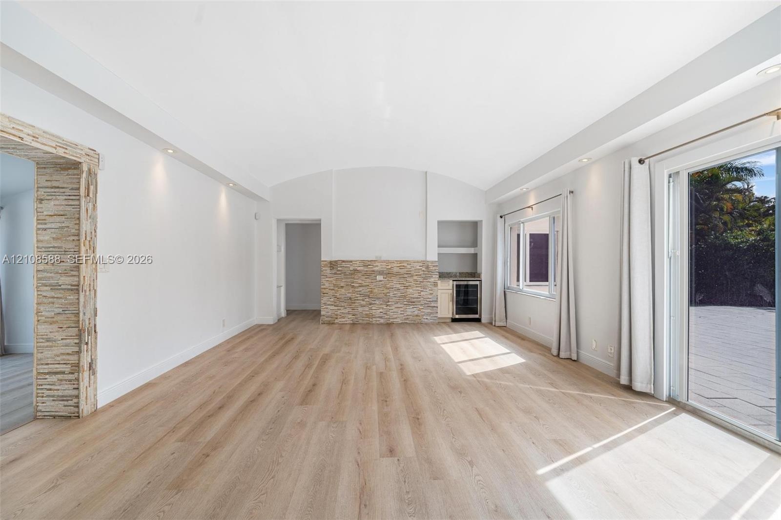 Vaulted ceiling featuring recessed lighting, stacked stone accent wall, integrated beverage refrigerator, and wood-finish flooring with sliding glass 