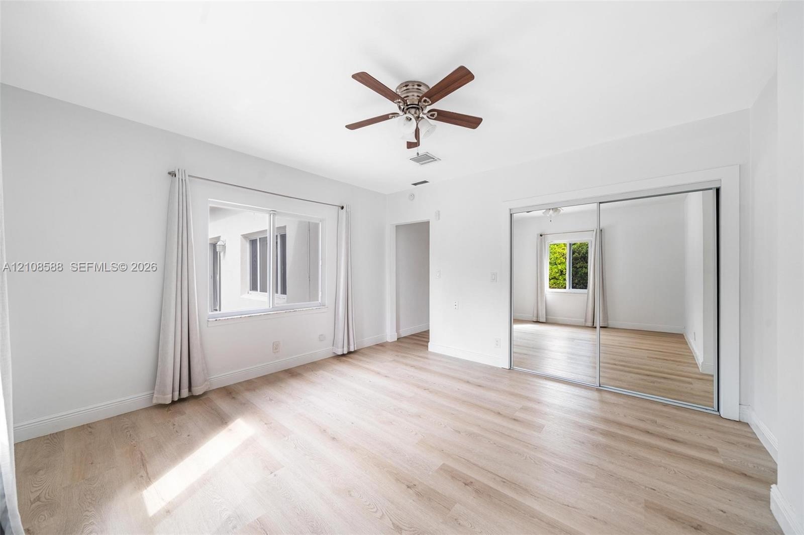 Wood-finish flooring, ceiling fan with integrated lighting, and sliding mirror-paneled closet doors