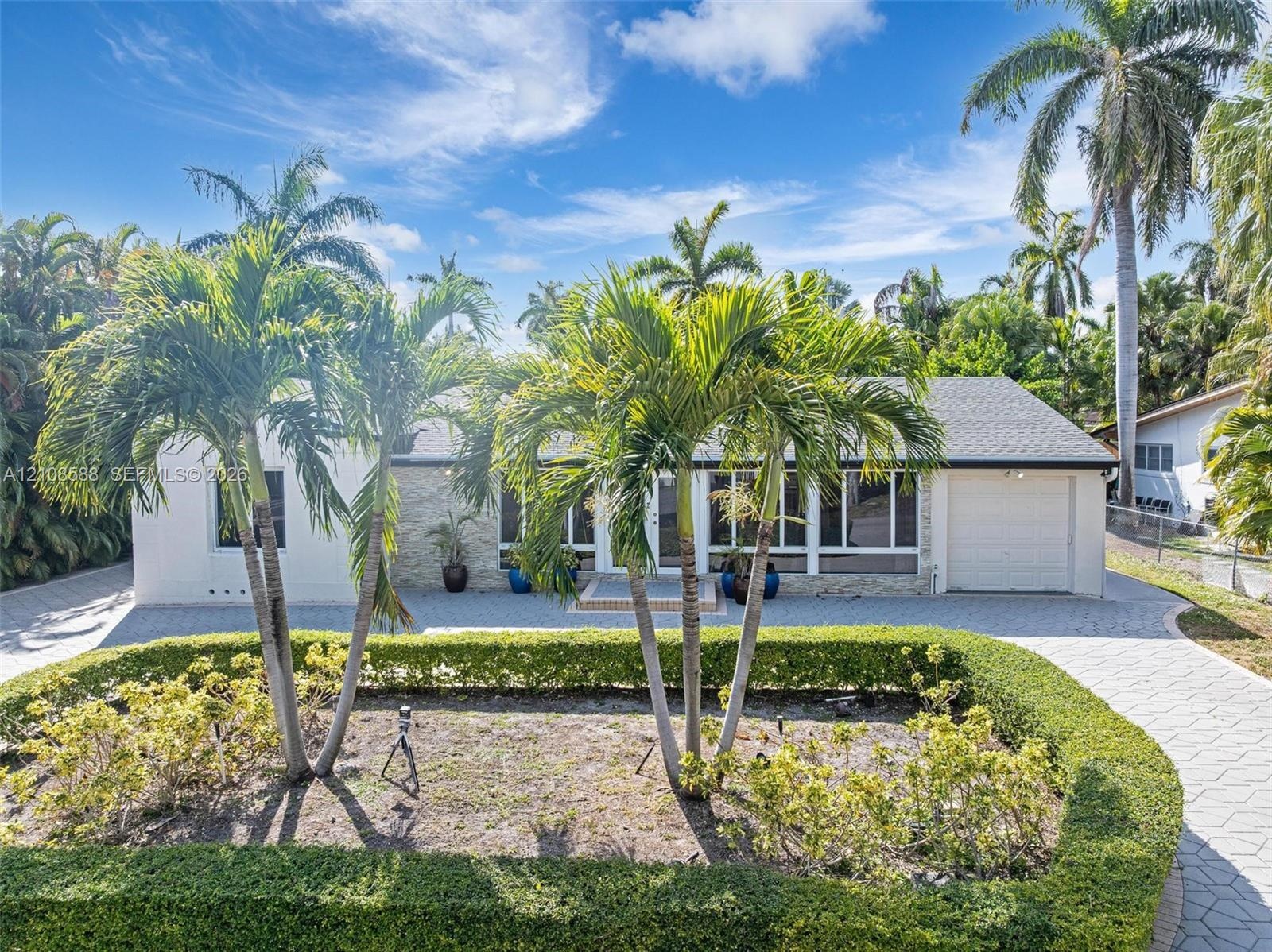 Single-story residence featuring a paved driveway, exterior stone veneer accents, multi-pane windows, attached garage, and mature landscaping with pal