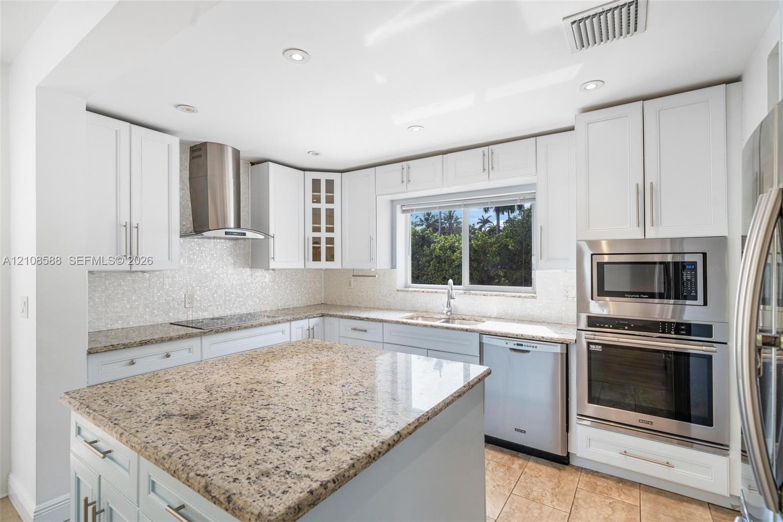 Kitchen featuring white cabinetry, stone countertops, stainless steel appliances including a built-in oven and microwave, mosaic tile backsplash, and 