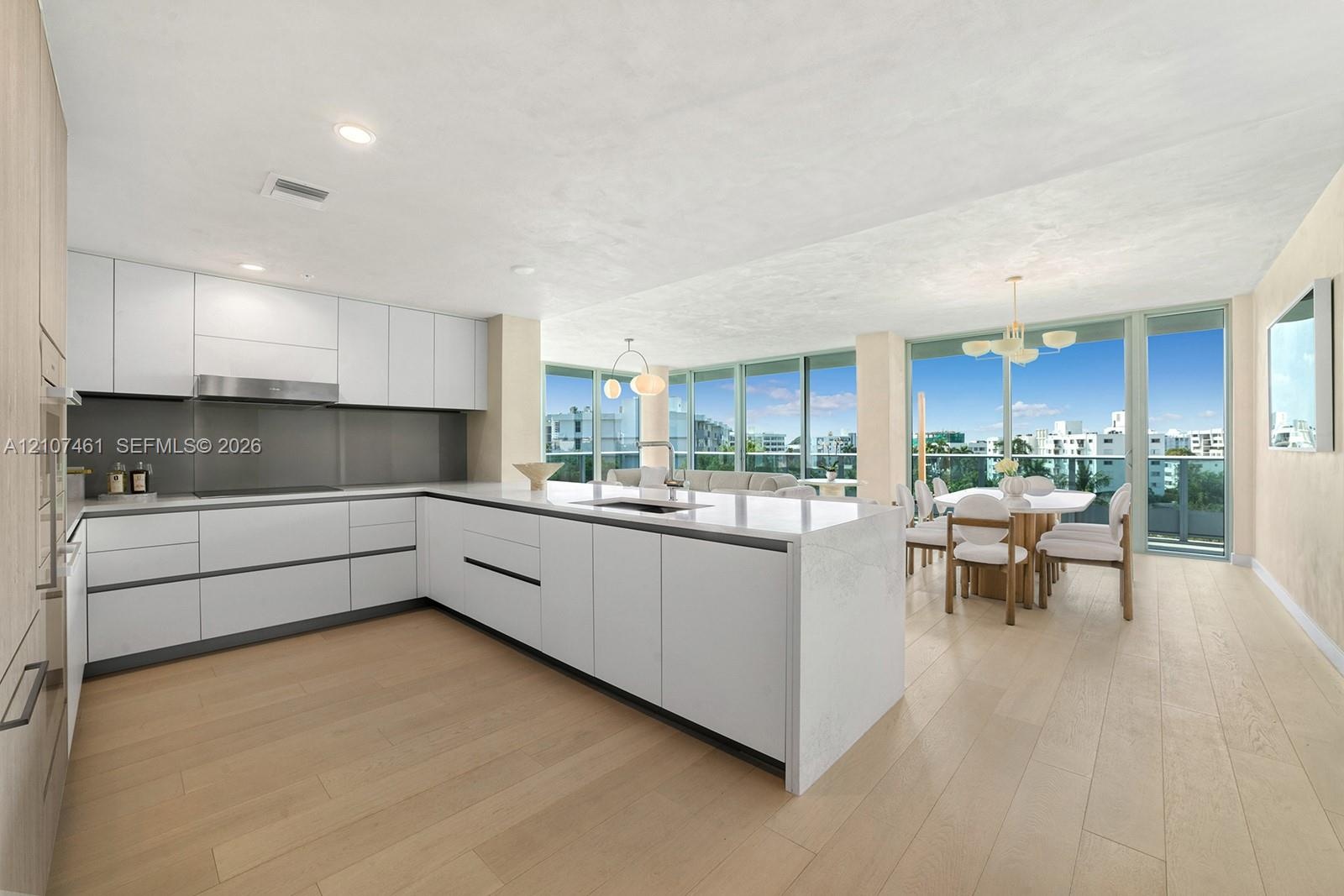 Contemporary kitchen featuring white handleless cabinetry, a substantial quartz-topped center island with integrated sink, stainless steel range hood,
