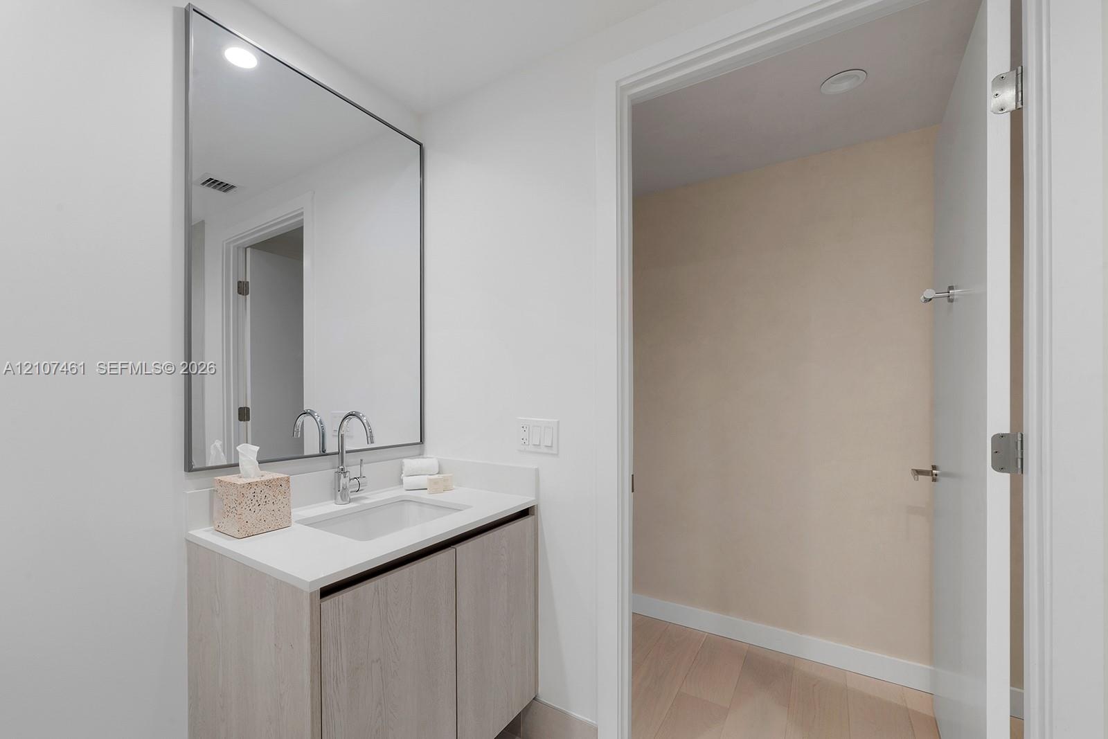 Bathroom vanity featuring light-toned cabinetry, a solid surface countertop with an integrated rectangular sink, a polished chrome bridge faucet, and 