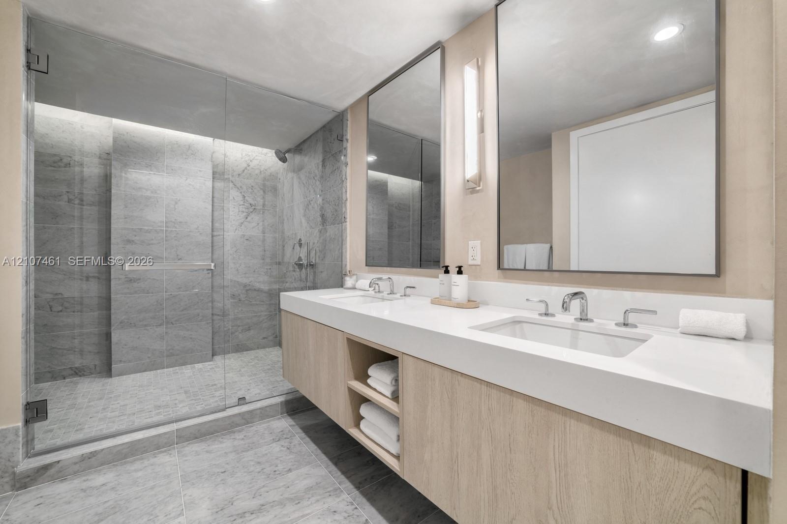 Floating dual vanity with integrated countertop, walk-in shower featuring glass enclosure and stone-tile surrounds, and rectangular wall-mounted mirro