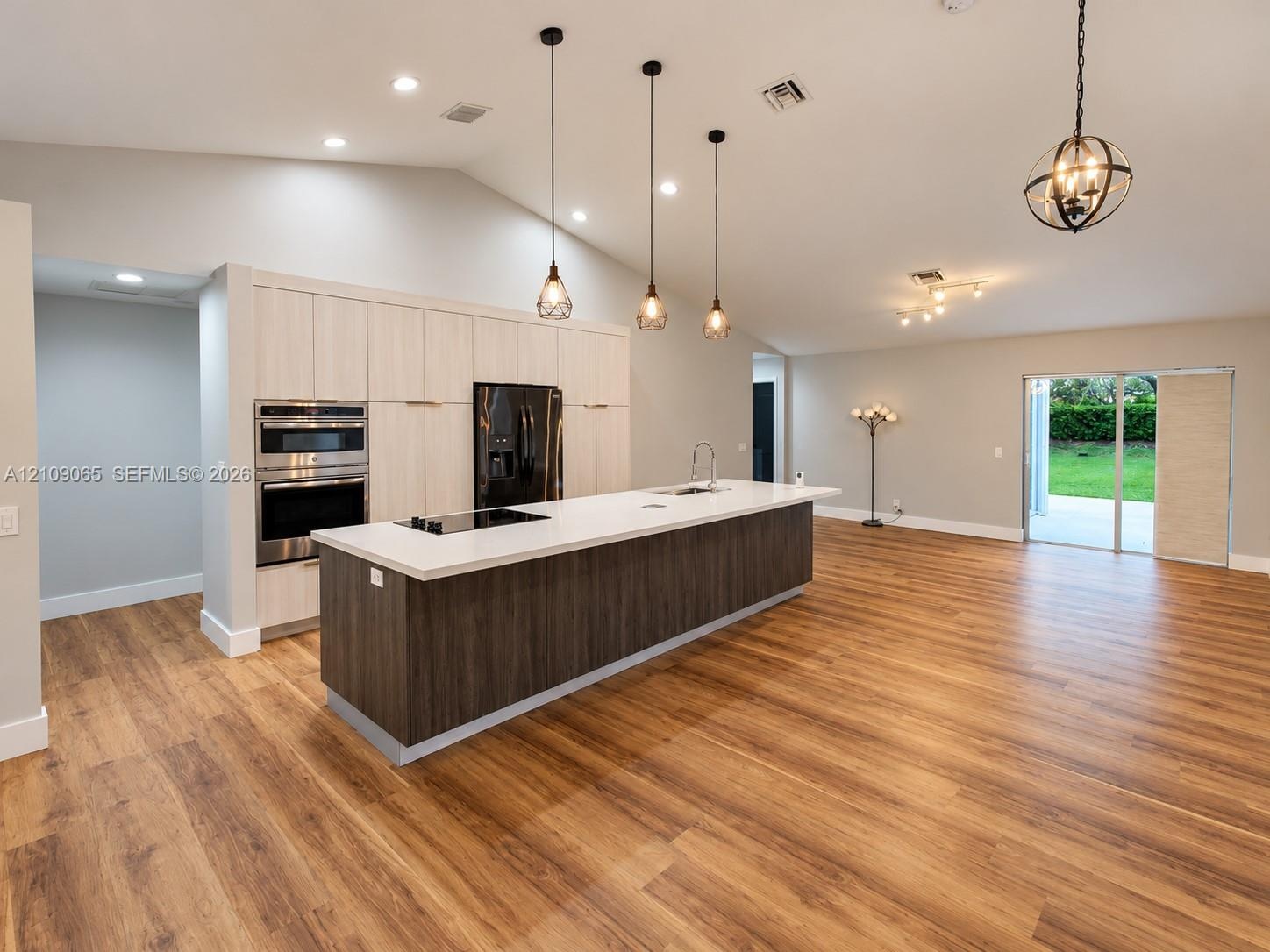 Open-concept kitchen featuring vaulted ceilings, wood-finish flooring, a central island with a solid surface countertop, light-toned cabinetry, and bu
