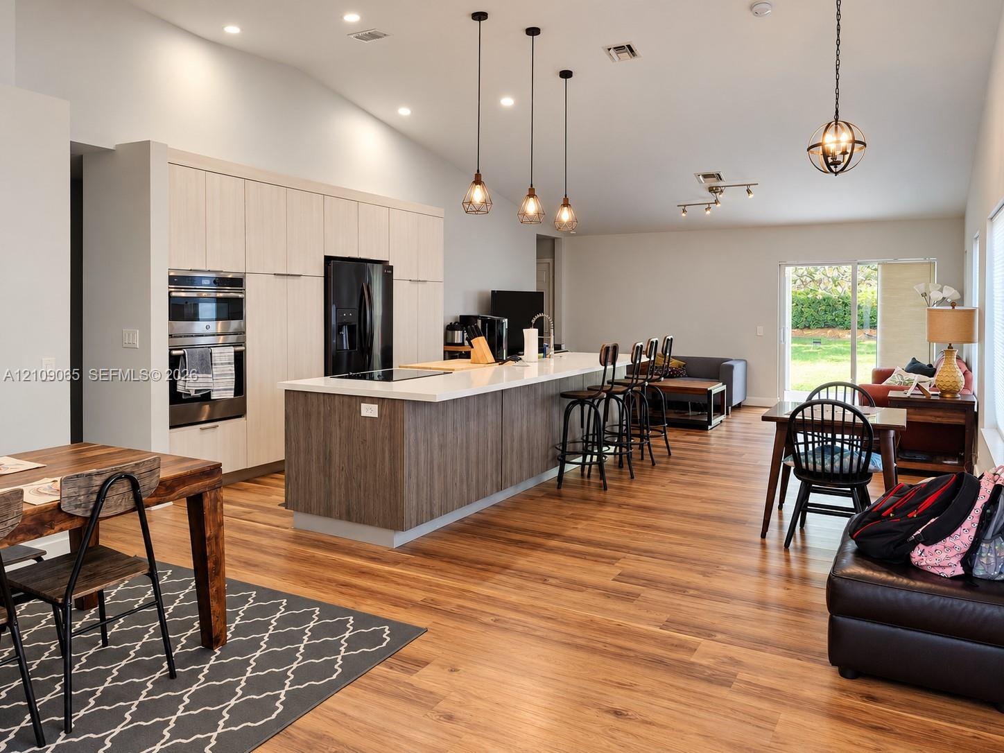 Open-concept kitchen featuring full-height light wood-finish cabinetry, a large center island with contrasting wood-finish paneling and quartz counter