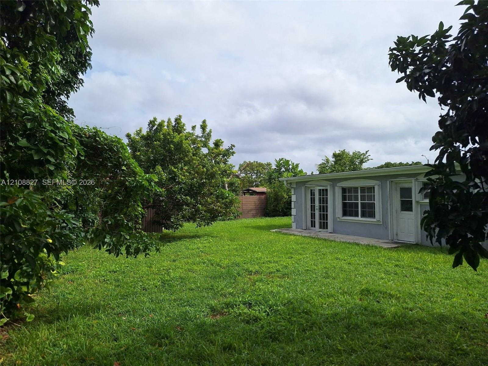 Expansive backyard featuring a lush grass lawn, mature foliage, perimeter privacy fencing, and exterior French doors