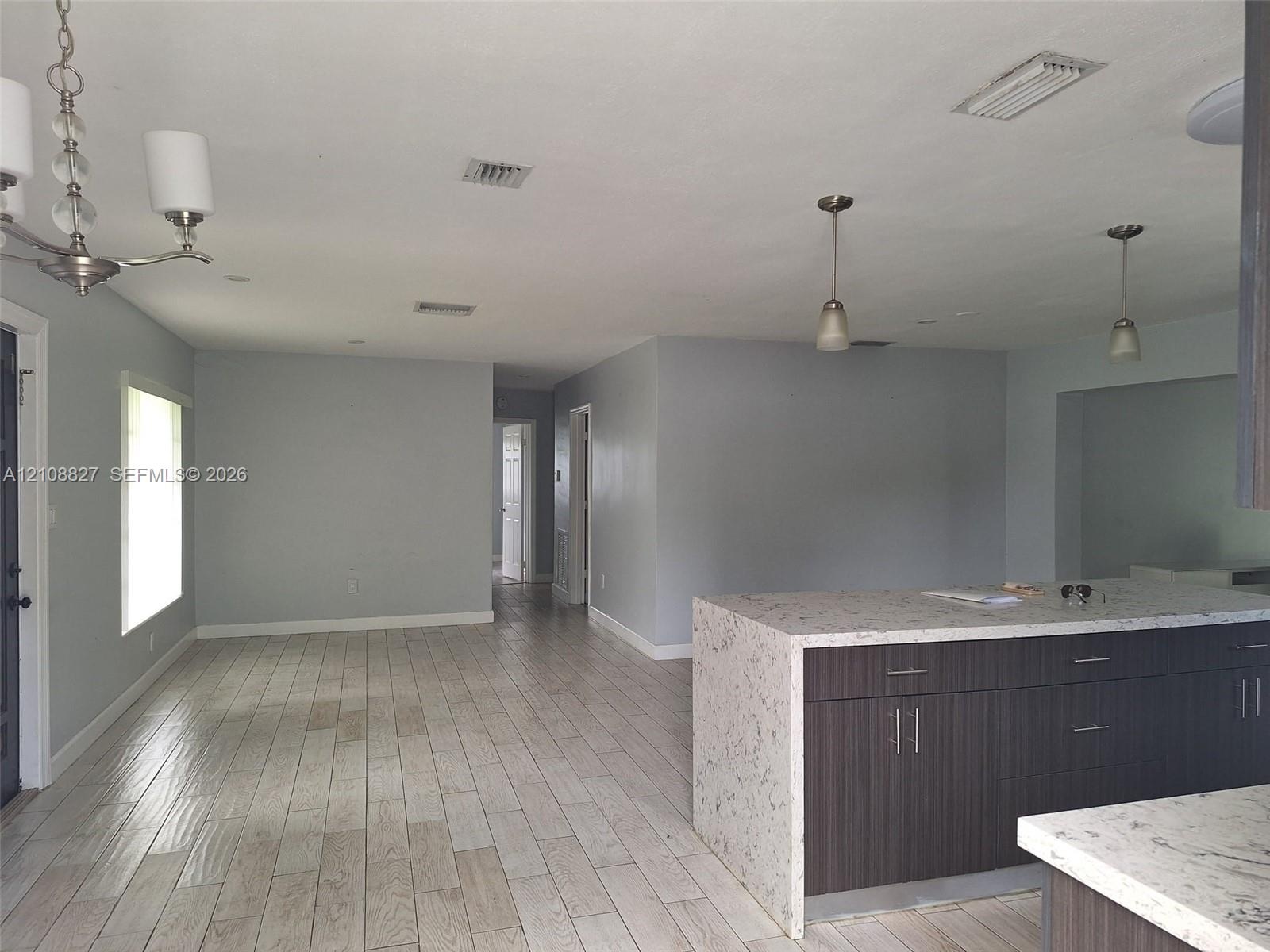 Kitchen featuring a central island with a stone-composite countertop, dark wood-finish cabinetry, neutral wall paint, wood-finish flooring, and pendan