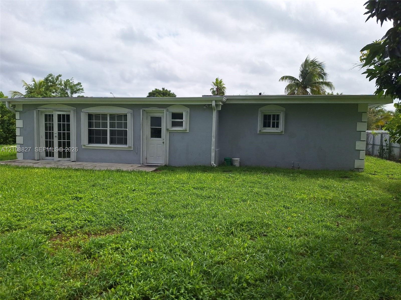 Single-story exterior featuring a concrete patio, white-trimmed grid windows, a glass-paneled entry door, and a grass-covered backyard