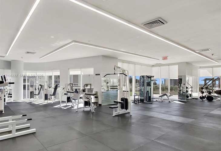 Fitness center featuring resilient rubber flooring, recessed architectural LED lighting, expansive floor-to-ceiling windows, and mirrored wall surface