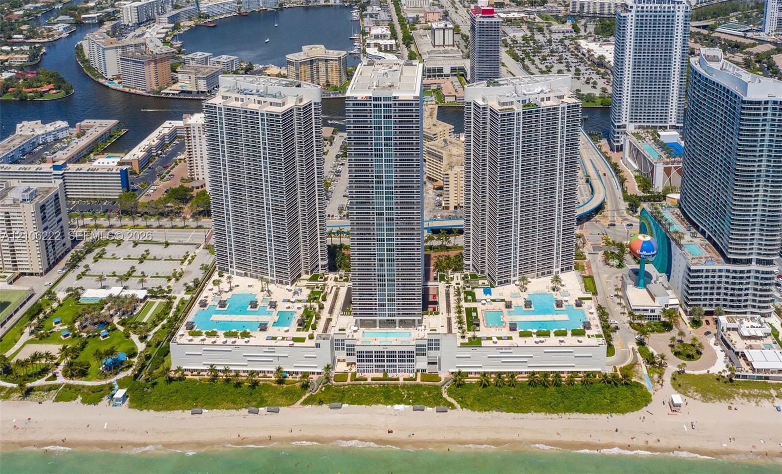 Aerial perspective of oceanfront high-rise residential complex featuring multiple swimming pools, spacious sun decks, extensive podium-level hardscapi