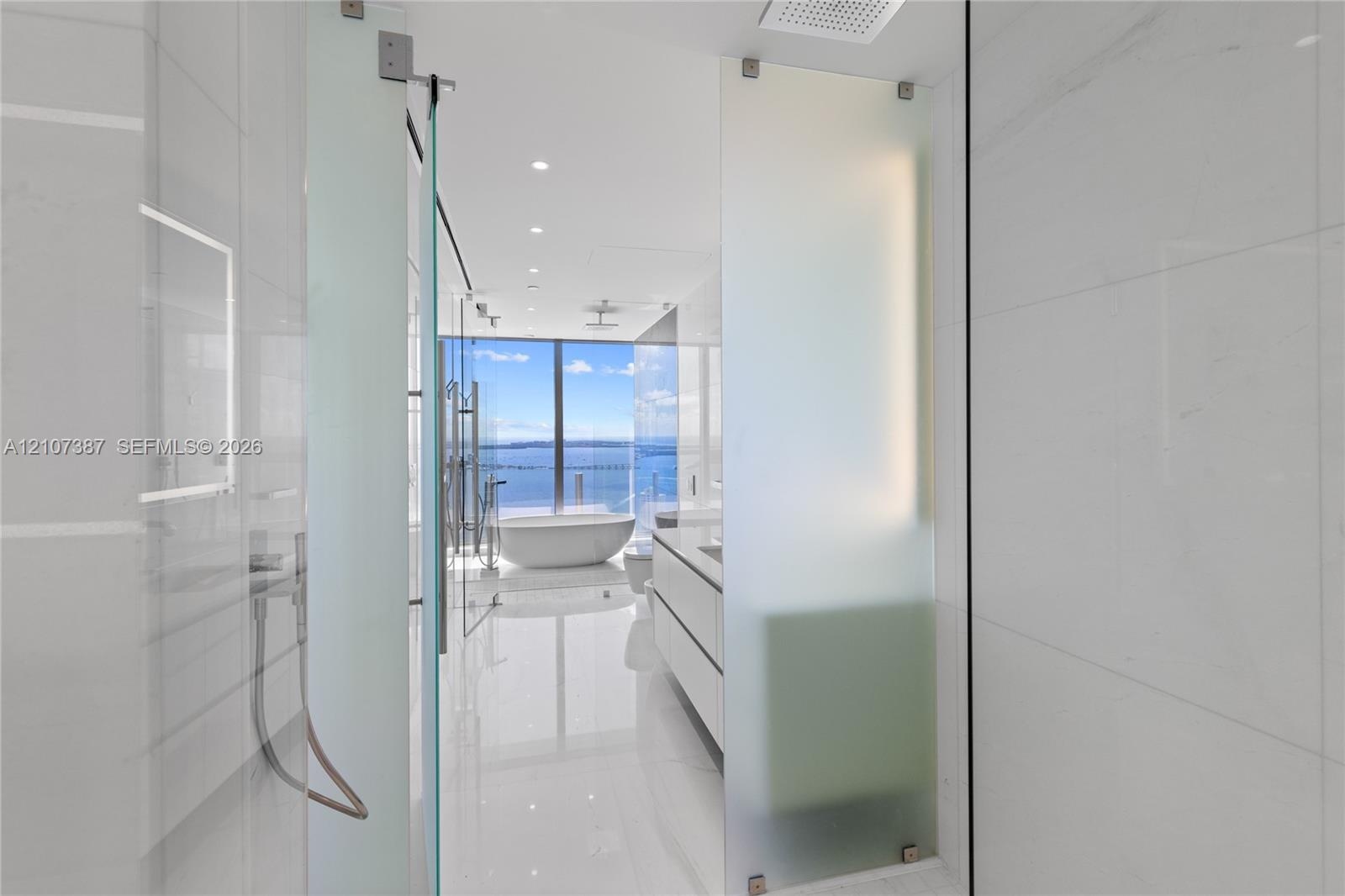 Floor-to-ceiling glass paneling, floating double vanity, freestanding soaking tub, large-format tile flooring, and integrated ceiling rain showerhead
