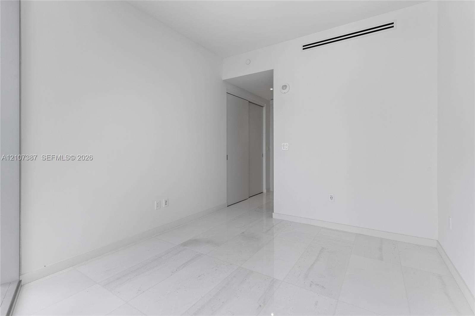 Minimalist interior space featuring polished light-toned stone flooring and dual-panel sliding closet doors