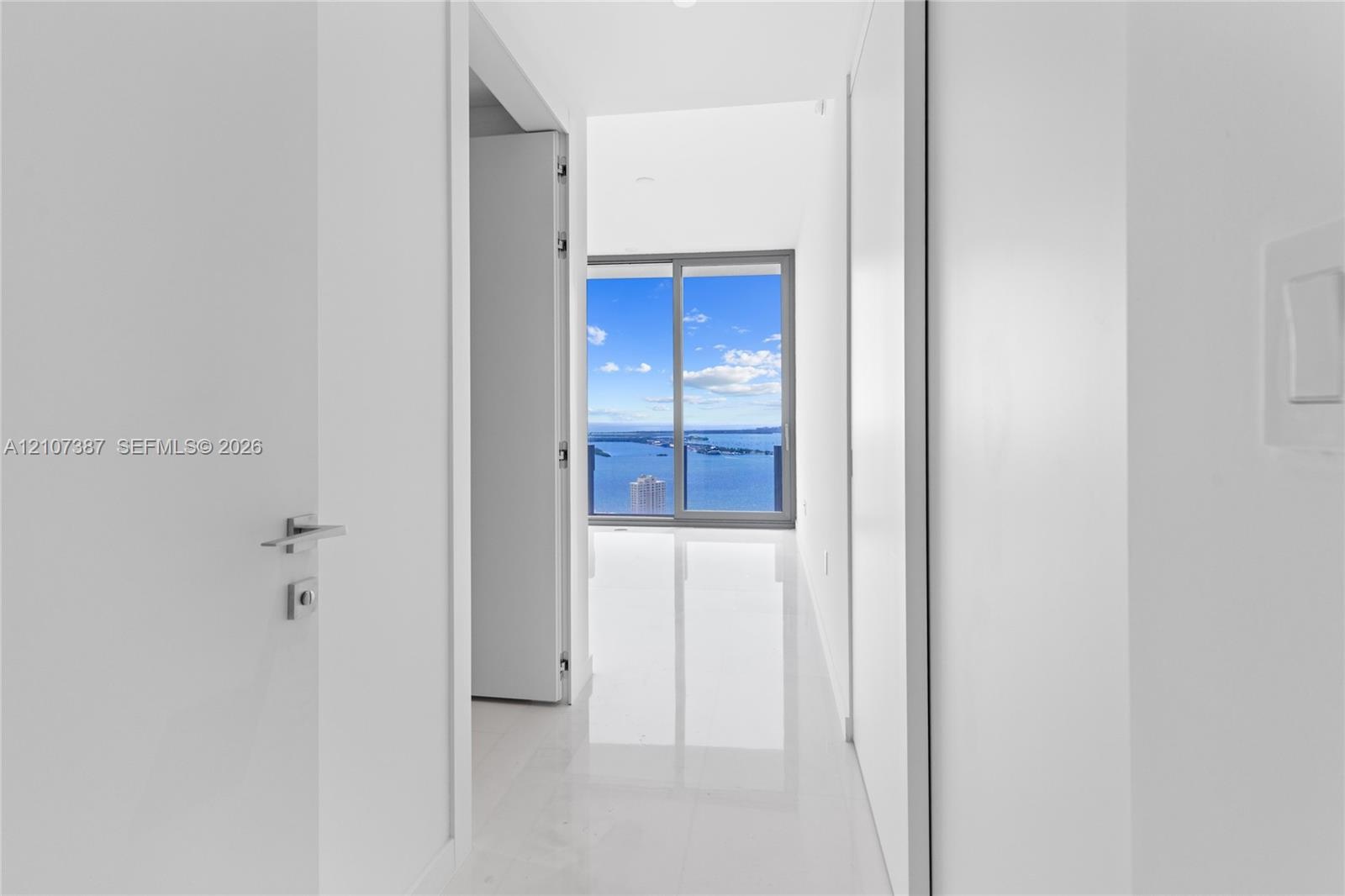 Hallway featuring polished white tile flooring, sleek flat-panel doors with contemporary hardware, and floor-to-ceiling sliding glass doors highlighti