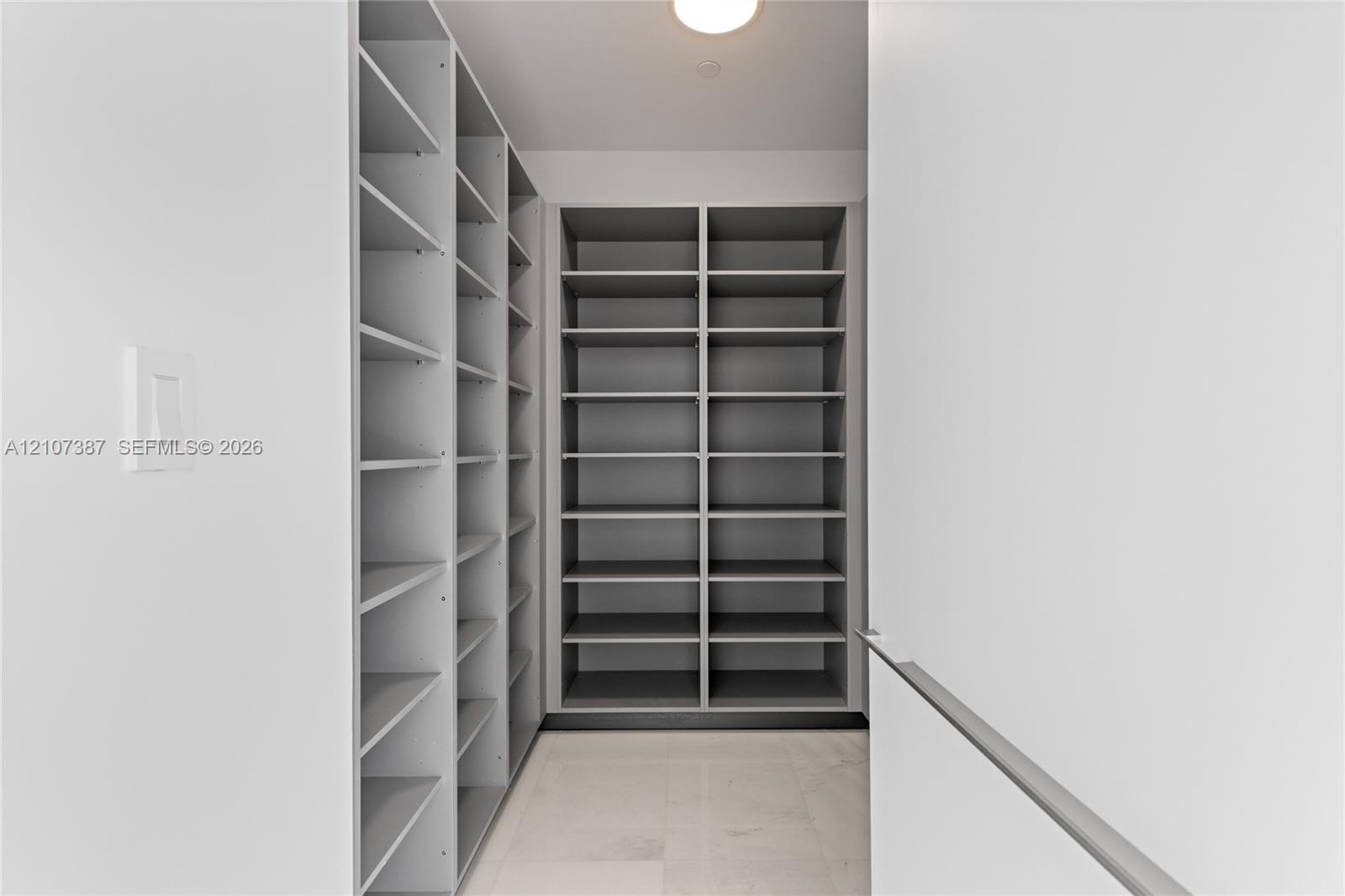 Custom walk-in storage featuring grey floor-to-ceiling shelving, light-toned tile flooring, and integrated overhead lighting