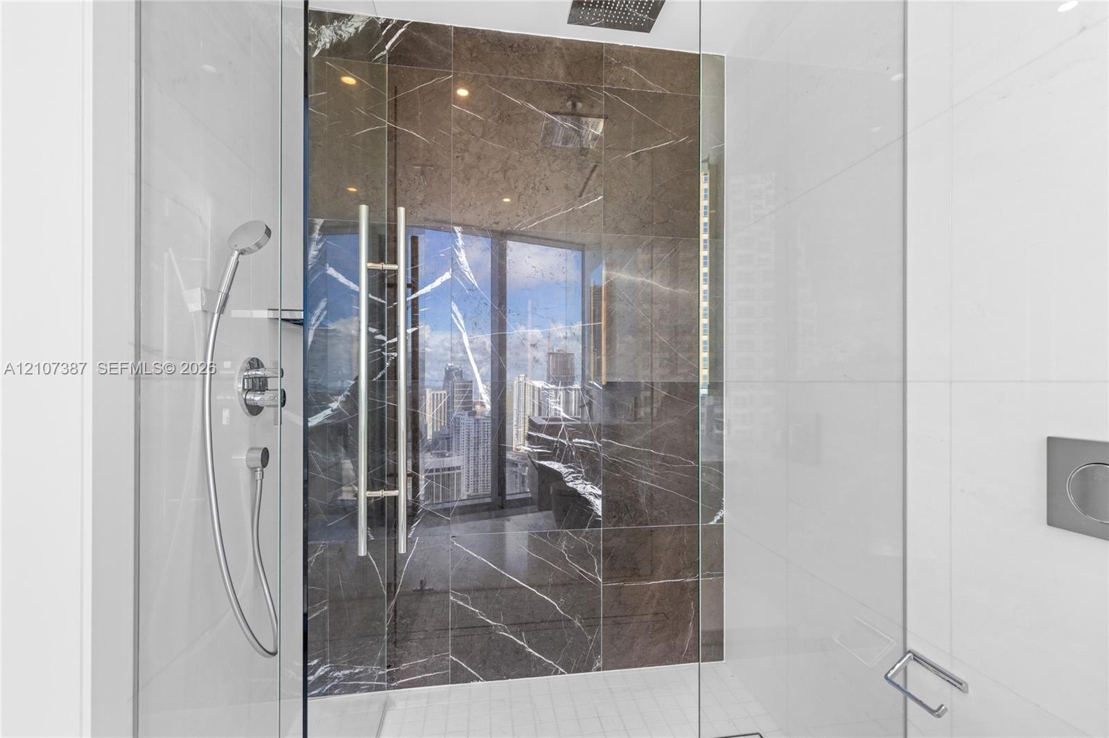 Walk-in shower featuring large-format dark stone tile accent wall, glass enclosure, ceiling-mounted rainfall showerhead, and integrated chrome handhel