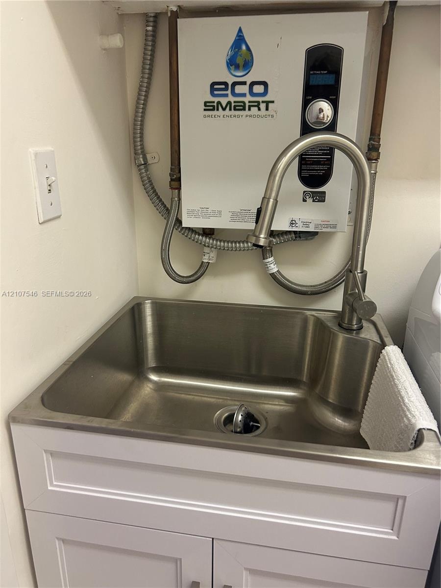 Stainless steel utility sink featuring a high-arc pull-down faucet, mounted above a white shaker-style vanity cabinet, accompanied by an electric tank