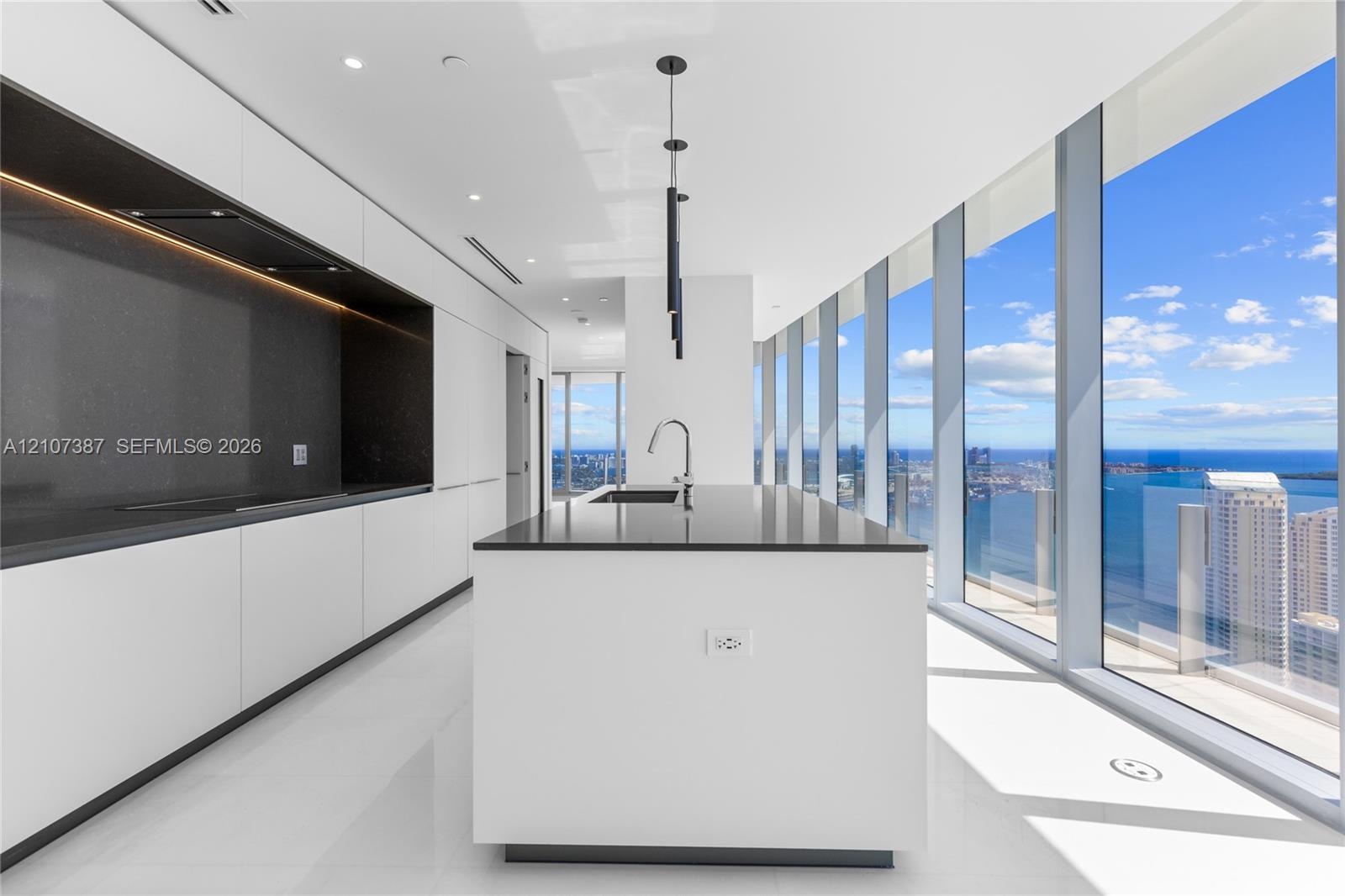 Contemporary kitchen featuring floor-to-ceiling windows, a center island with a dark stone countertop, minimalist flat-panel cabinetry, integrated rec