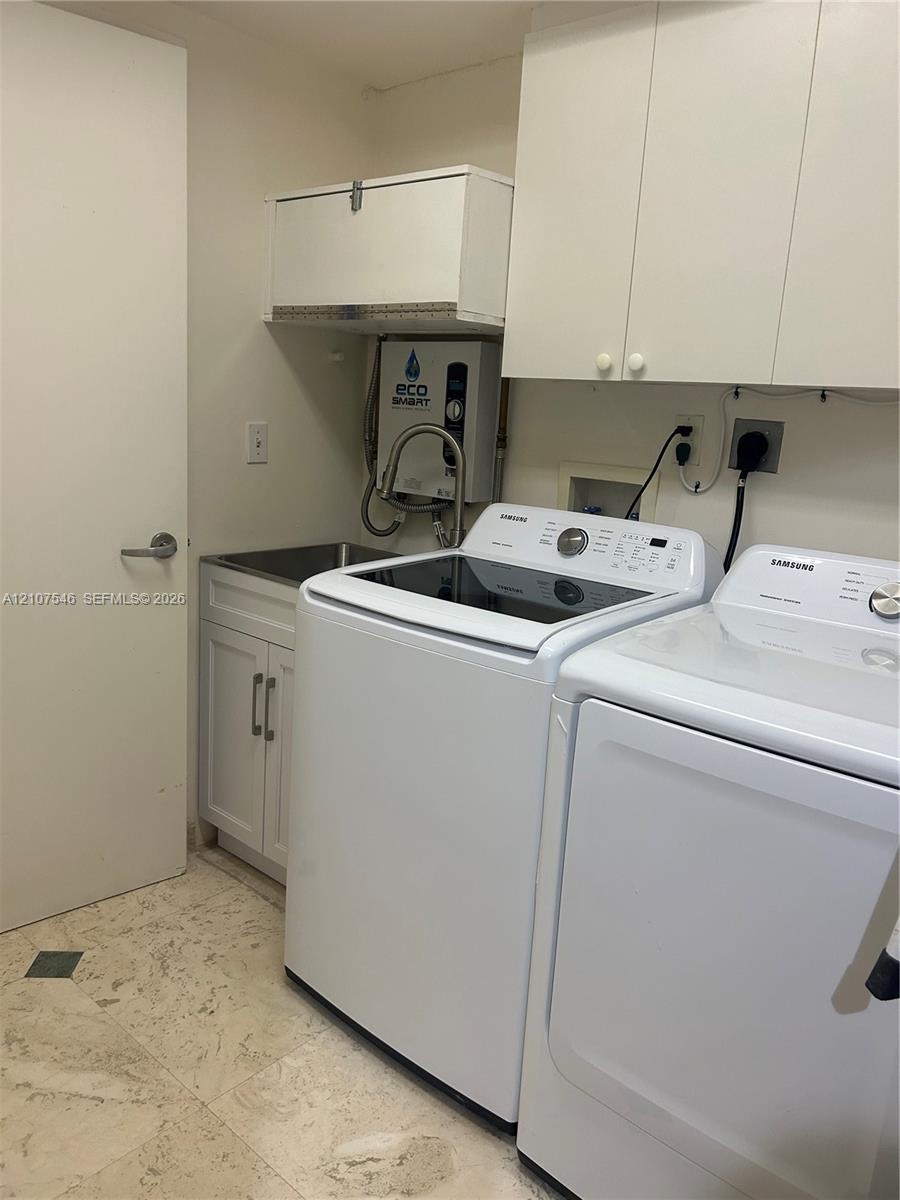 Utility area featuring white shaker-style cabinetry, wall-mounted storage units, a stainless steel sink with a high-arc pull-down faucet, and stone fl