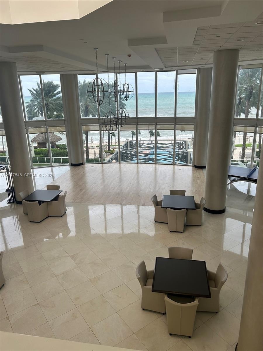 Double-height floor-to-ceiling windows, polished tile flooring, wood-finish flooring accents, structural cylindrical columns, and metal orb pendant li
