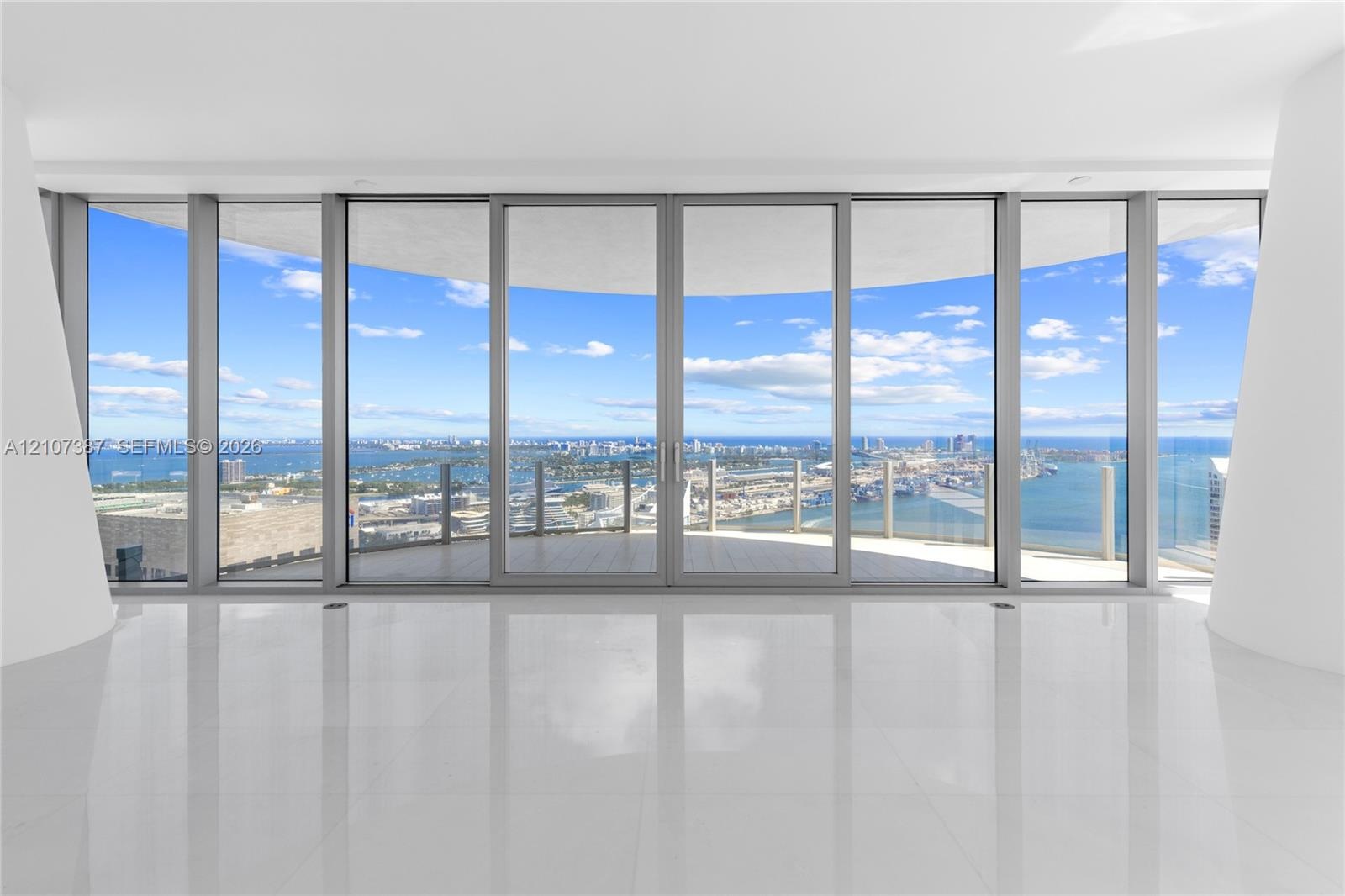 Floor-to-ceiling glass walls, expansive curved balcony with a glass railing, polished tile flooring, and structural white pillars