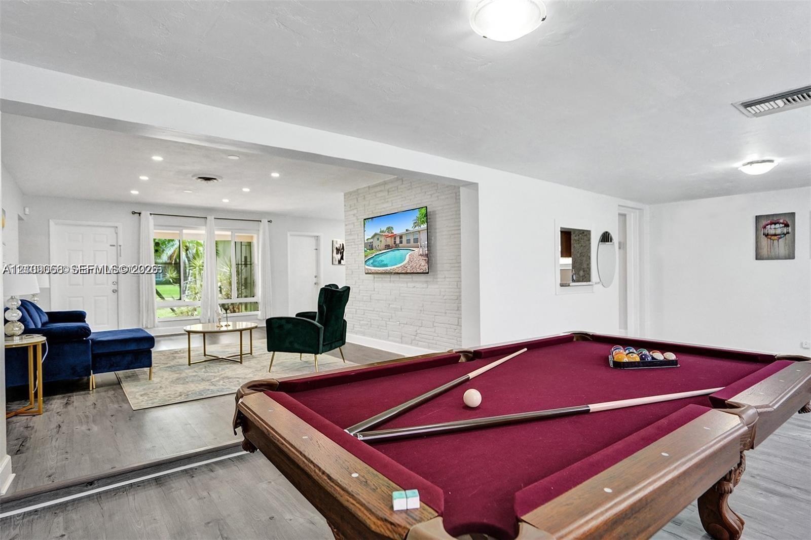 Open-concept living space featuring wood-finish flooring, a white-painted brick accent wall, recessed lighting, and expansive glass paneled exterior d