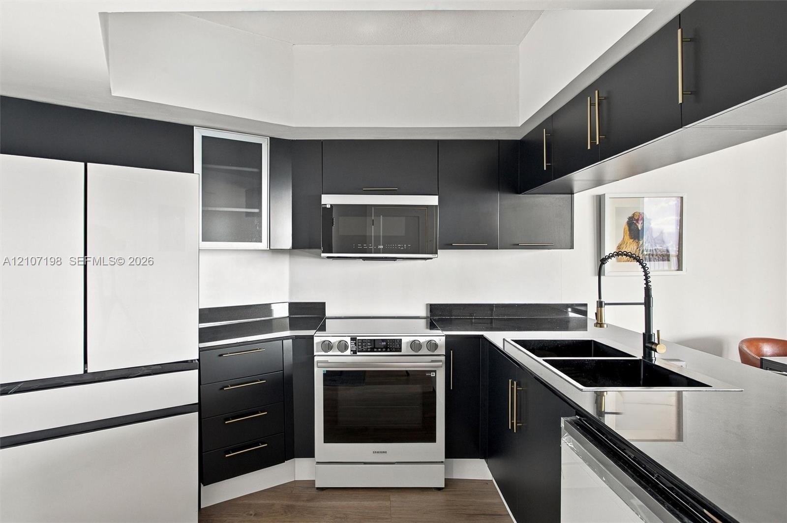 Modern kitchen featuring matte black cabinetry with gold-toned hardware, dark stone countertops, an integrated microwave, a high-arc faucet, and wood-