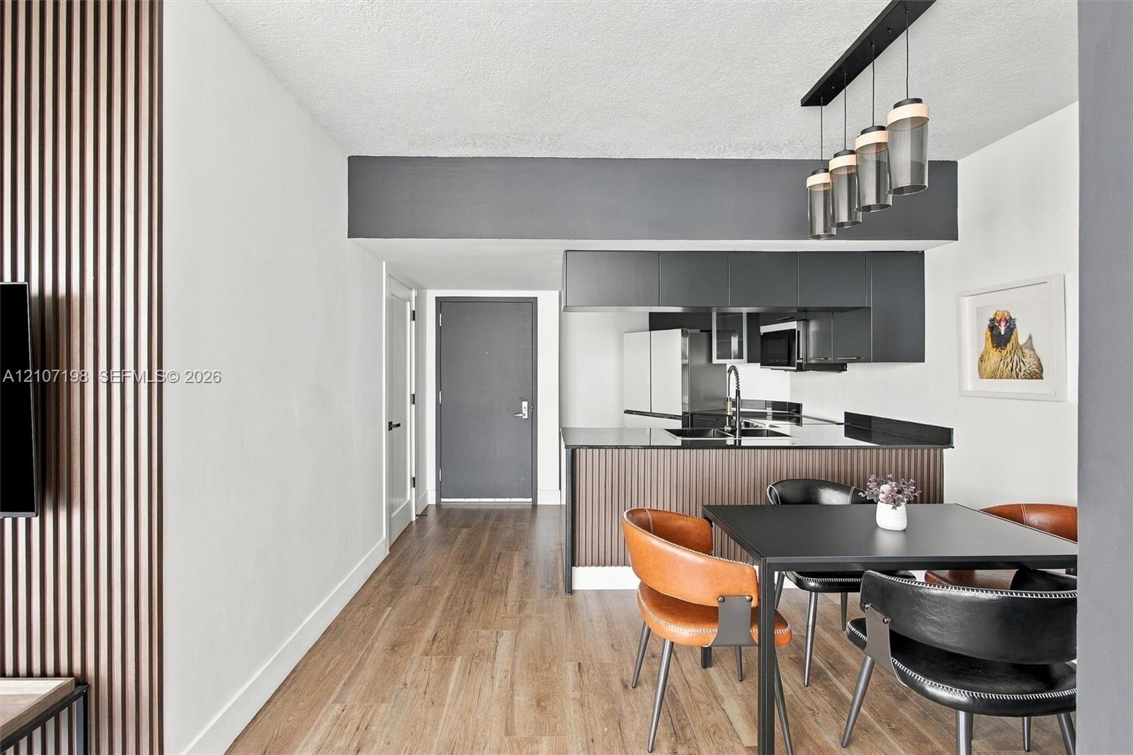 Interior featuring wood-finish flooring, vertical slat wall paneling, matte black cabinetry, a peninsula with dark-toned counters, and a modern multi-