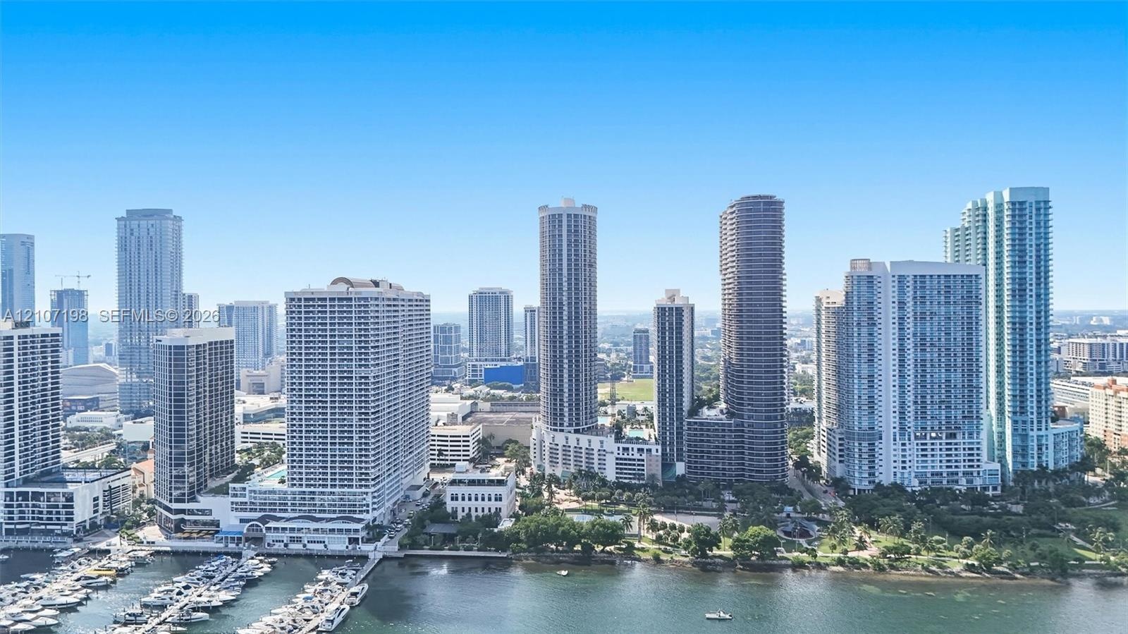 High-rise urban landscape featuring a dense skyline of multi-story glass-facade buildings, a waterfront marina with boat slips, and interspersed areas