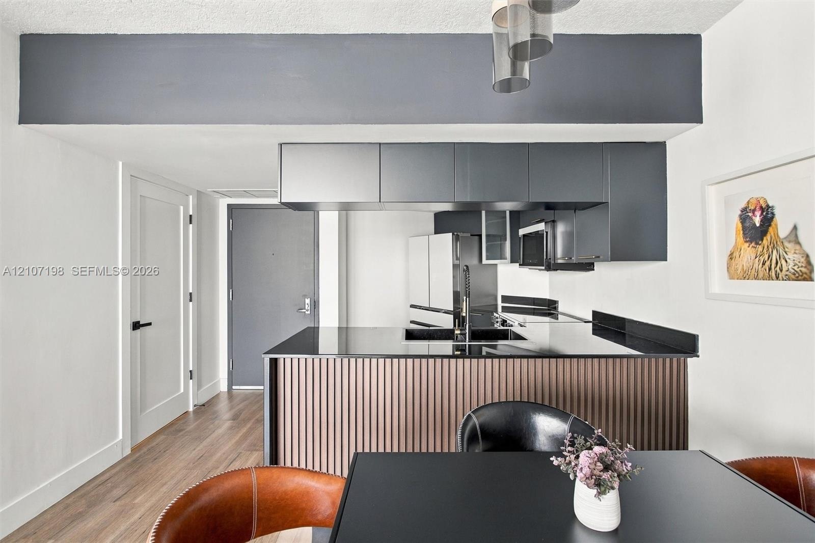 Kitchen featuring matte grey cabinetry, black countertops, wood-finish slat paneling on the island, wood-finish flooring, and multi-pendant lighting