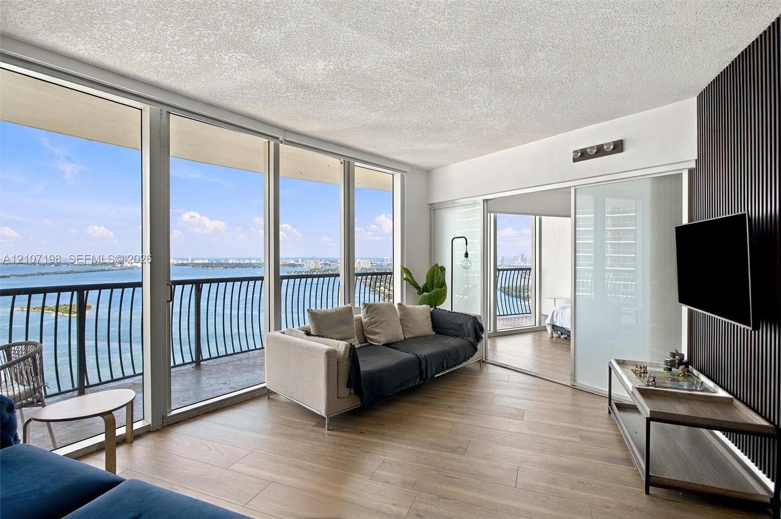 Floor-to-ceiling windows, wood-finish flooring, balcony with metal railing, and a dark vertical-slat accent wall