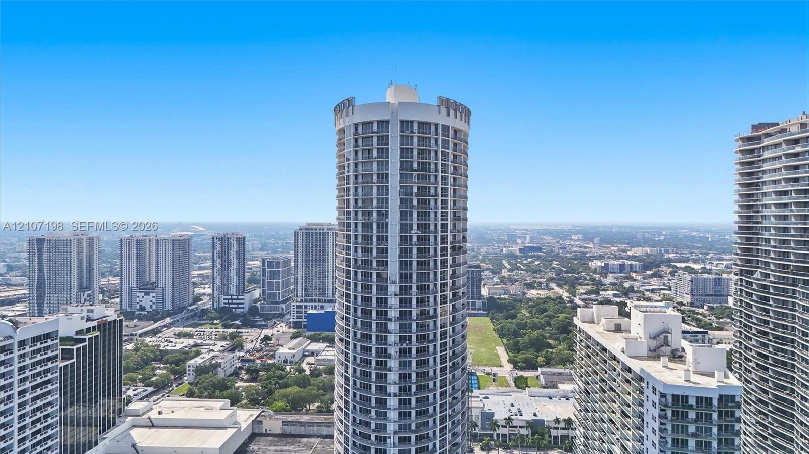 Cylindrical high-rise architecture featuring a white concrete facade, multi-story glass-paned balconies, and a repeating grid of floor-to-ceiling wind