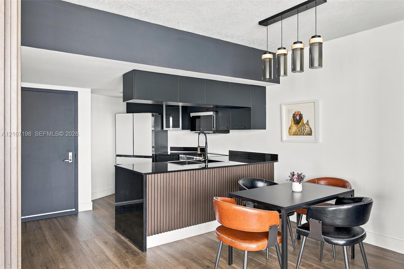 Kitchen featuring matte black cabinetry, contrasting dark stone countertops, a fluted-panel island, wood-finish flooring, and a multi-pendant light fi