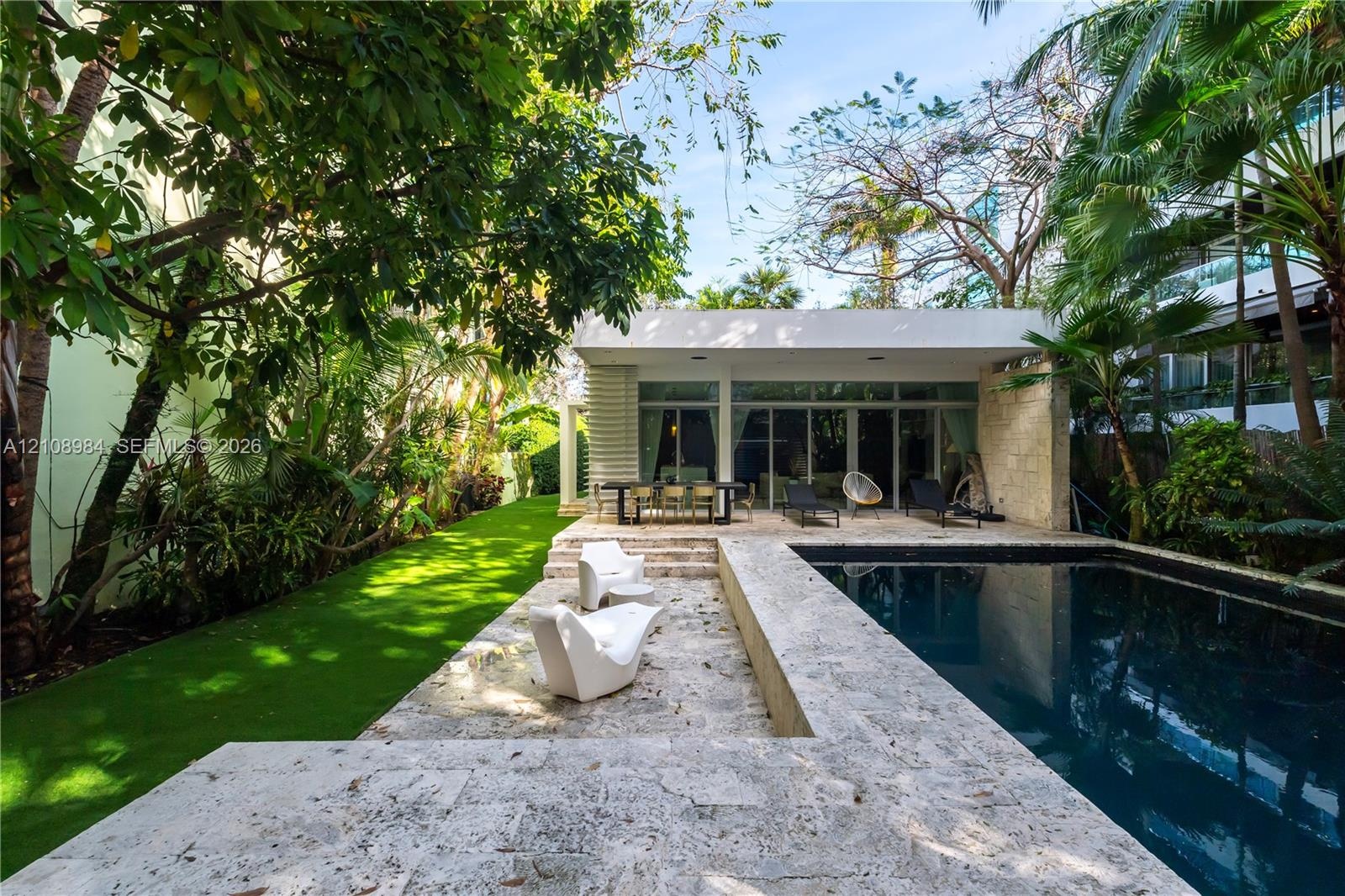 Outdoor living area featuring a custom swimming pool with stone decking, integrated landscape design, and a flat-roofed structure with floor-to-ceilin