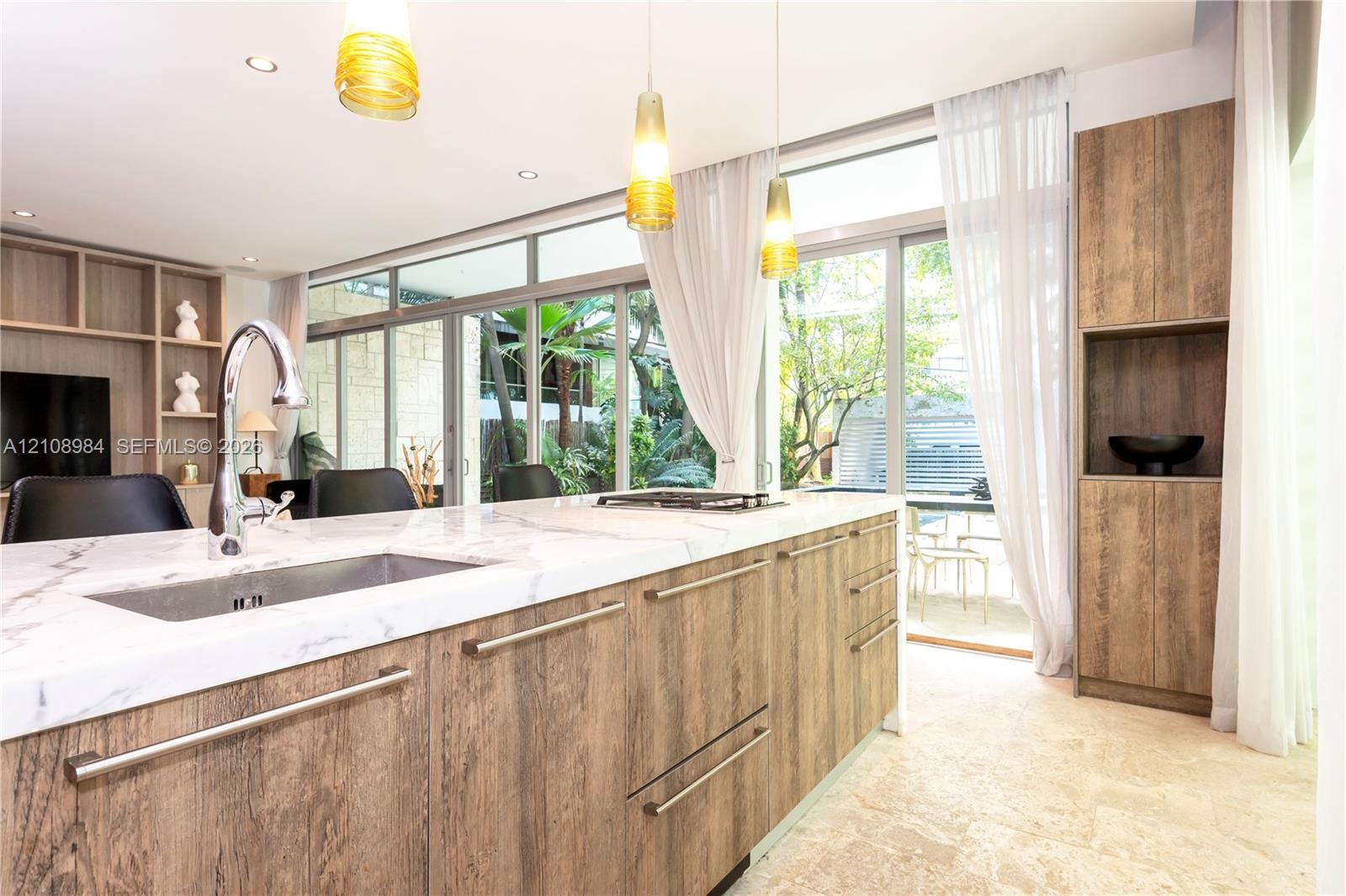 Kitchen island featuring a stone-surface countertop, integrated under-mount sink, wood-finish cabinetry, floor-to-ceiling glass sliding doors, and pen