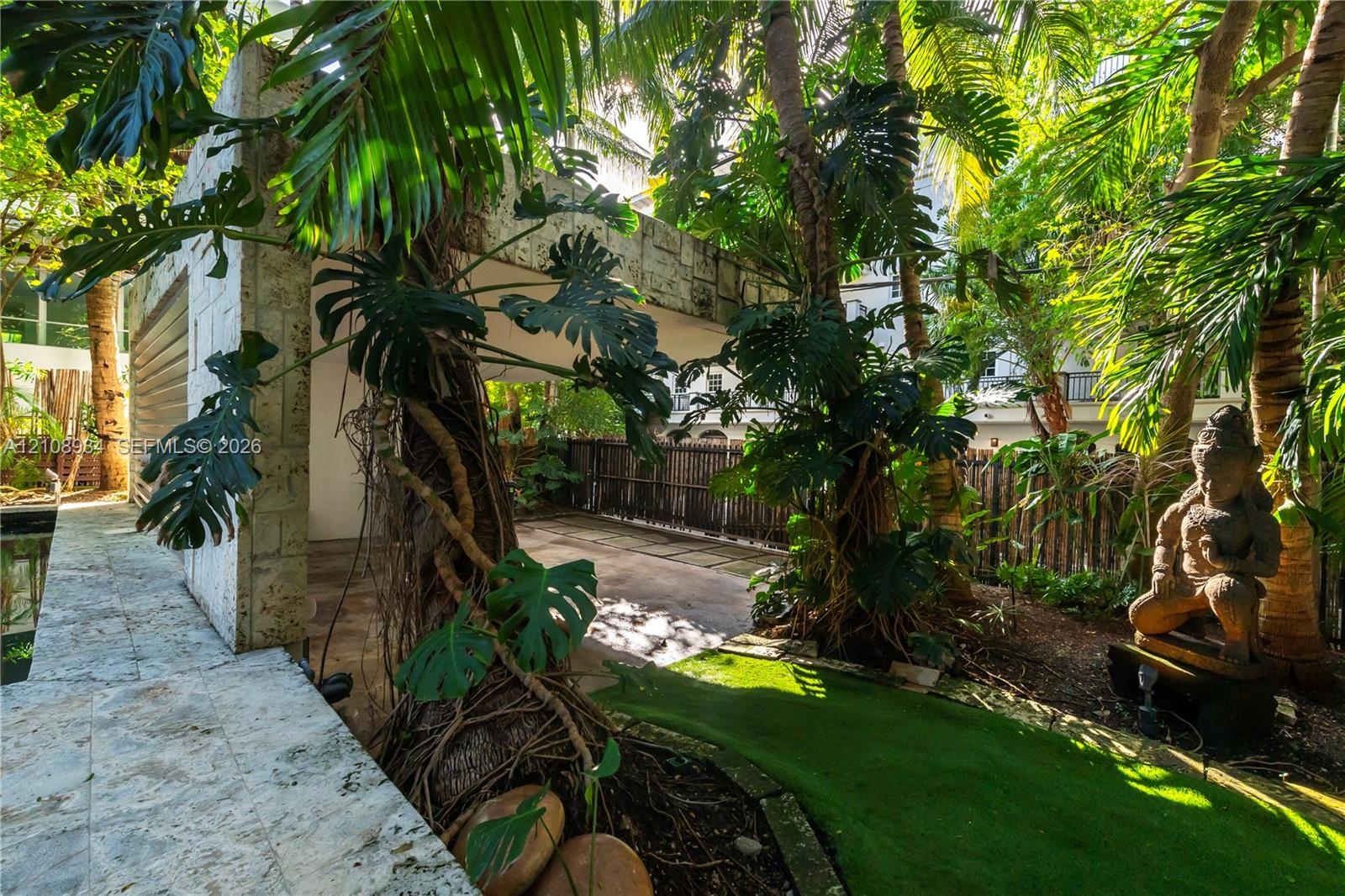 Outdoor area featuring stone-clad structural pillars, natural stone paving, mature tropical landscaping, and a built-in privacy fence