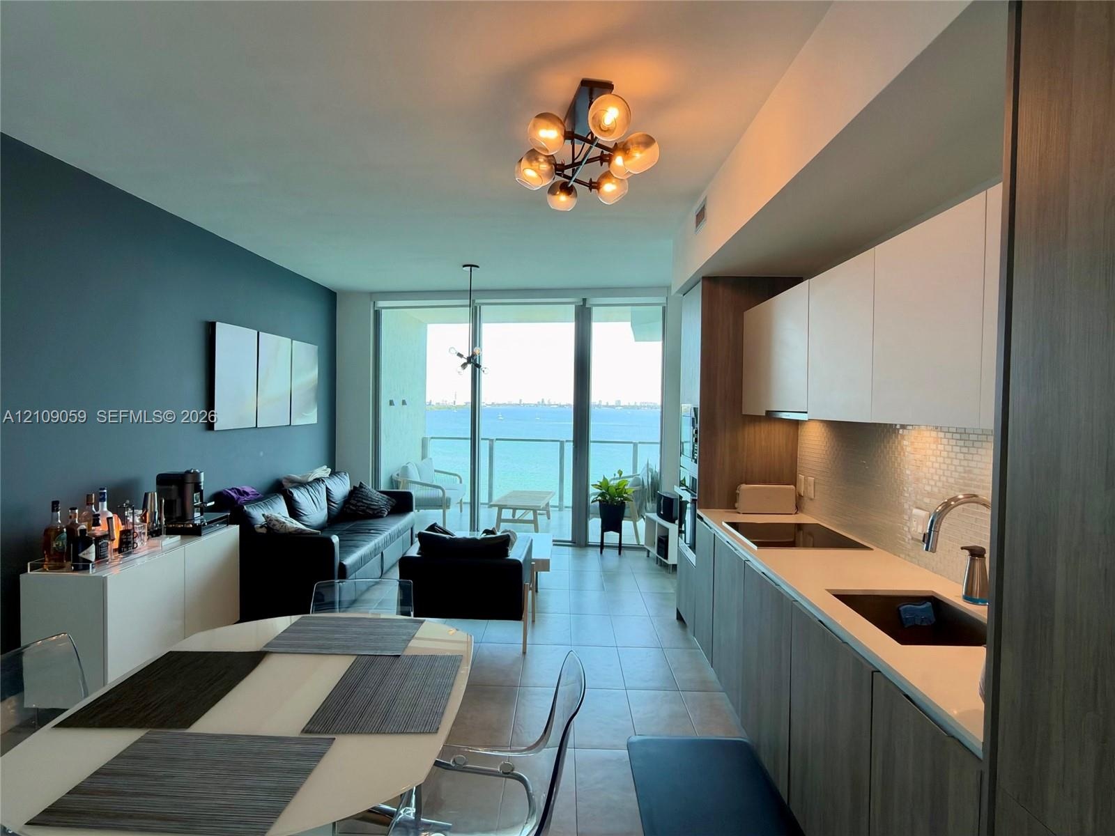 Kitchen featuring flat-panel cabinetry, light-toned countertops, tile backsplash, and floor-to-ceiling glass doors opening to a balcony