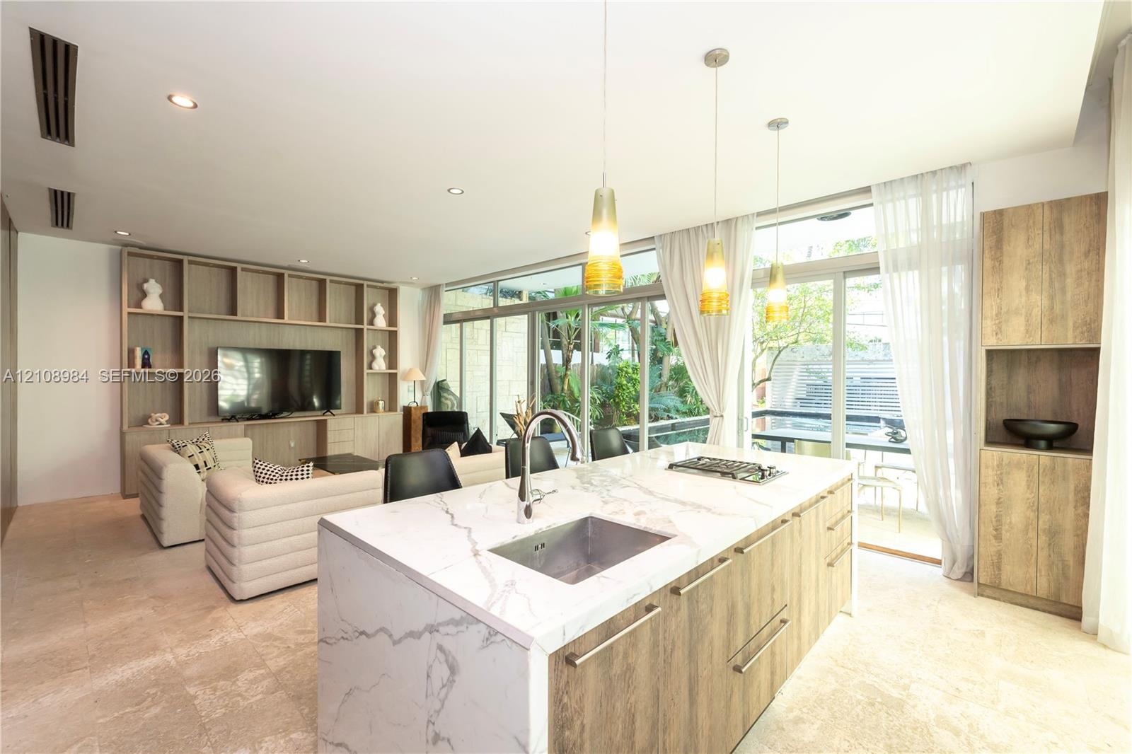 Open-concept kitchen featuring an island with a stone-finish countertop, undermount sink, and integrated stovetop, complemented by floor-to-ceiling wo