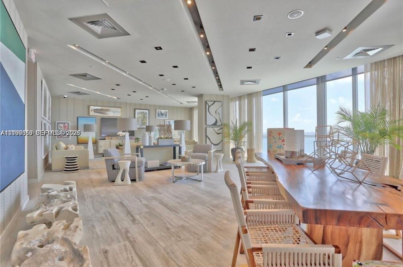 Open-concept living space featuring floor-to-ceiling windows, recessed architectural lighting, wood-finish flooring, and a coffered ceiling design