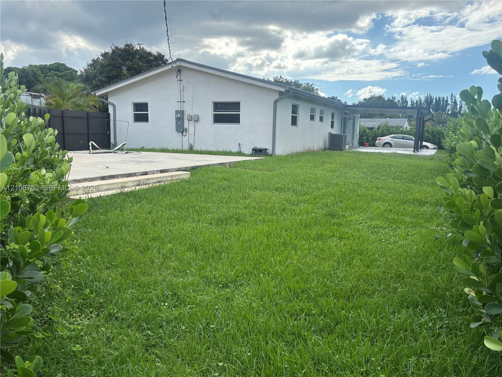 Spacious rear lawn featuring a concrete patio, covered side terrace, and perimeter privacy fencing