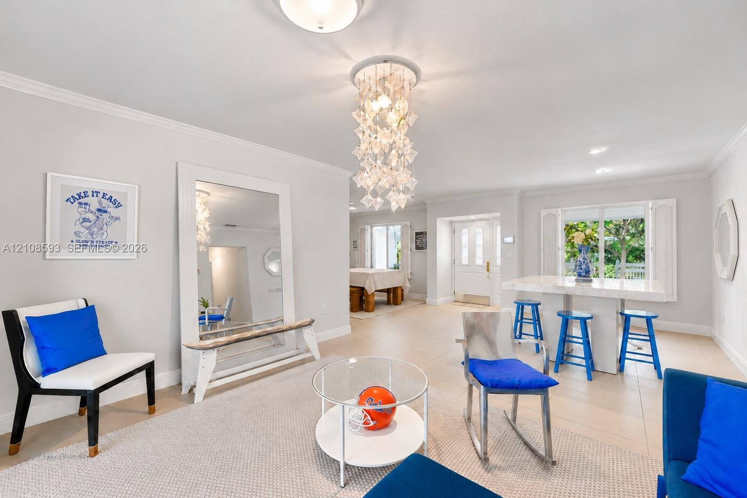 Open-concept interior featuring large-format tile flooring, a multi-tiered crystal-style chandelier, decorative crown molding, and a built-in stone-to