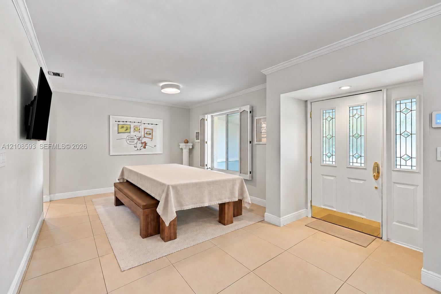 Entryway featuring neutral-tone tile flooring, crown molding, and a white front door with decorative glass inserts, brass hardware, and a matching sid
