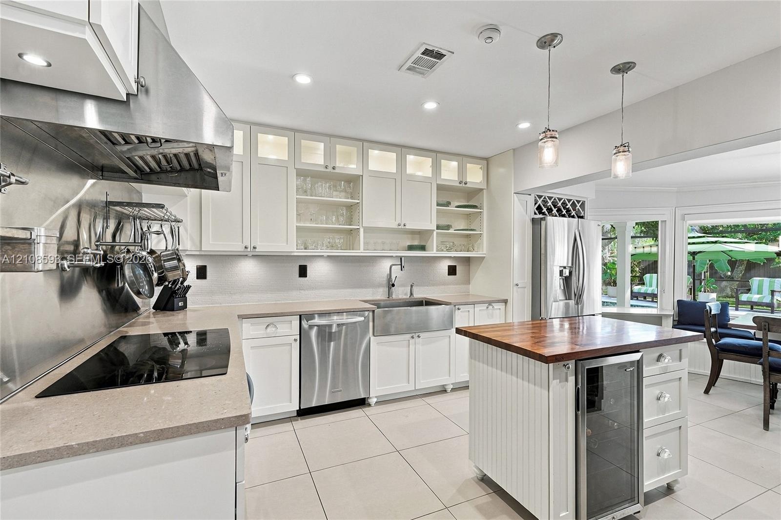 Kitchen featuring white cabinetry with glass-front uppers, stainless steel farmhouse sink, professional-grade range hood, butcher-block topped island 