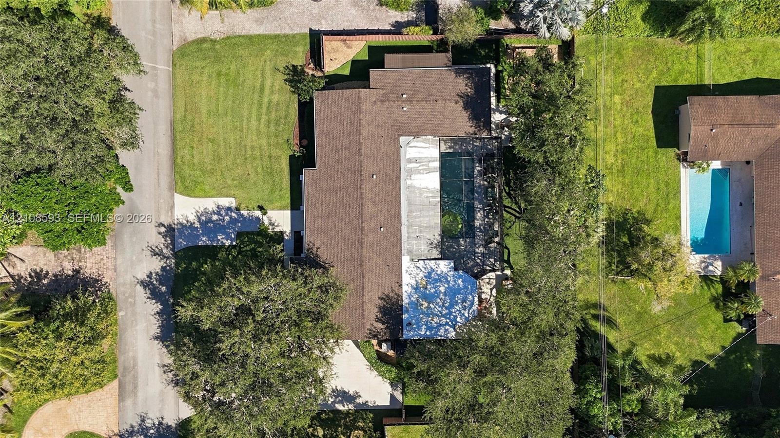 Aerial perspective featuring a multi-pitched shingle roof, paved driveway, expansive lawn, and mature trees