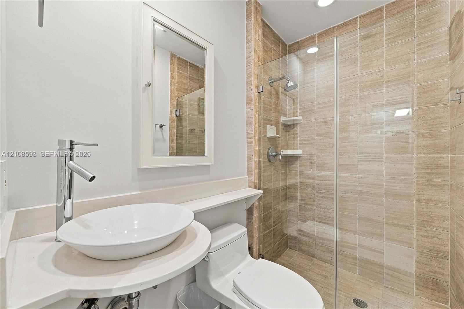 Bathroom featuring a white oval vessel sink, chrome high-arc faucet, solid surface countertop, walk-in shower with floor-to-ceiling tile, and frameles
