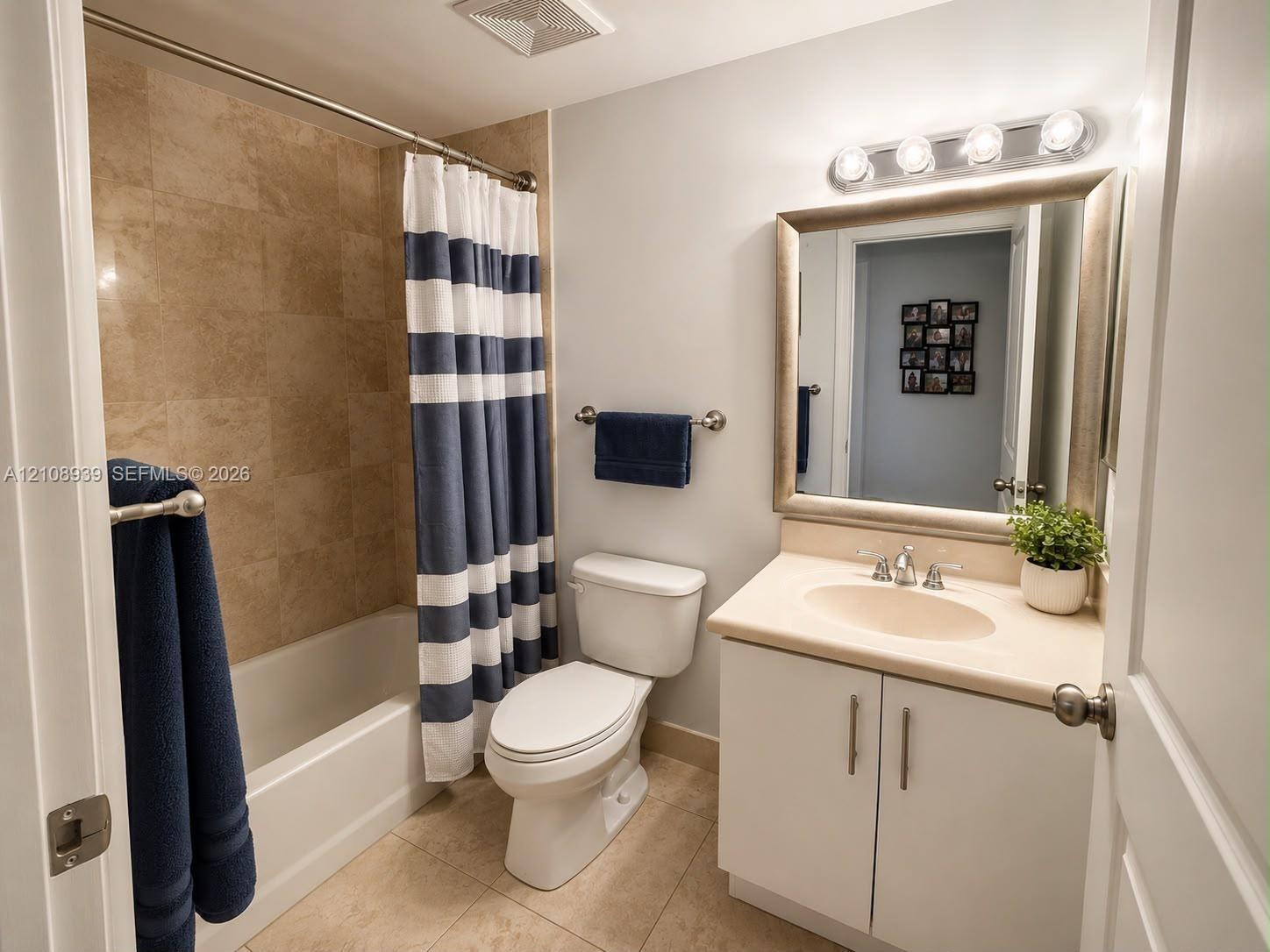 Bathroom featuring tile-surround bathtub, solid-surface vanity countertop, white cabinet storage, ceramic tile flooring, and wall-mounted vanity light