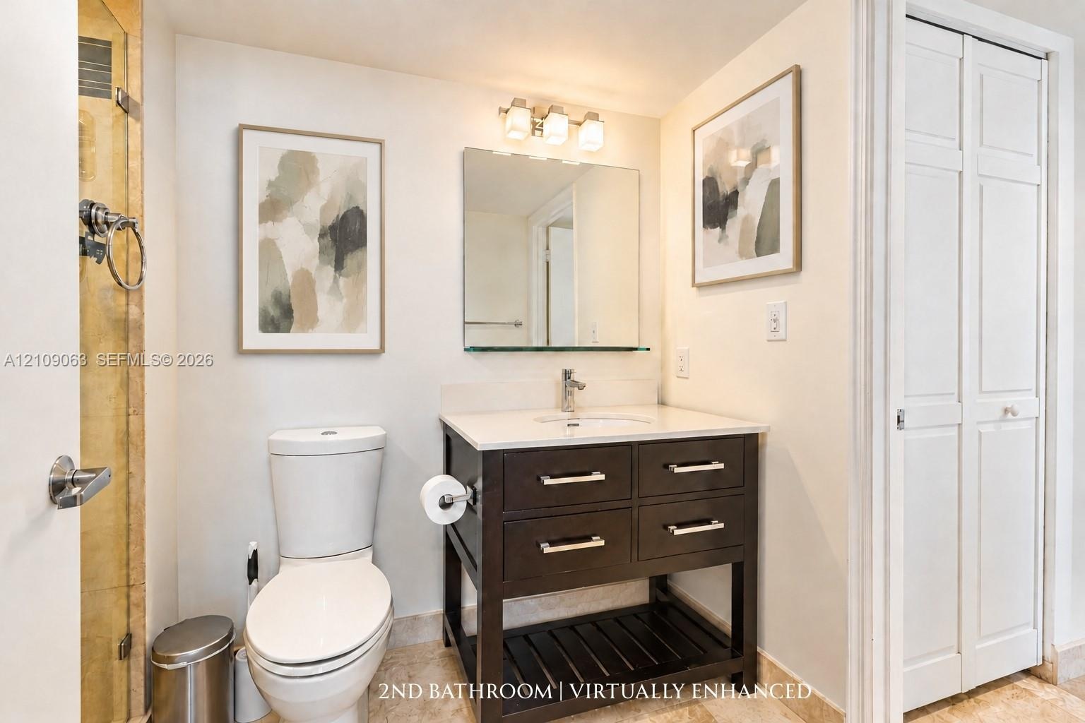 Vanity with a stone countertop and integrated sink, dark-finish cabinetry with silver-tone hardware, glass-enclosed shower, wall-mounted mirror, and t