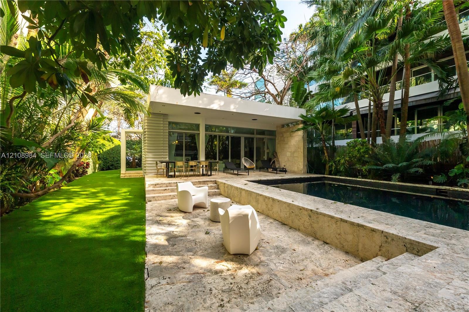 Outdoor terrace featuring natural stone paving, rectangular swimming pool, manicured lawn, and mature palm trees