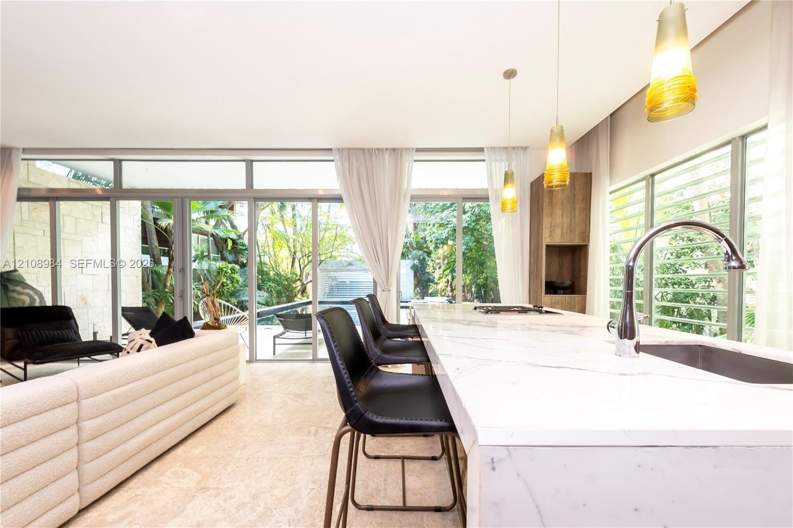 Kitchen island featuring a waterfall-edge stone countertop, undermount sink, and chrome gooseneck faucet, complemented by floor-to-ceiling glass panel