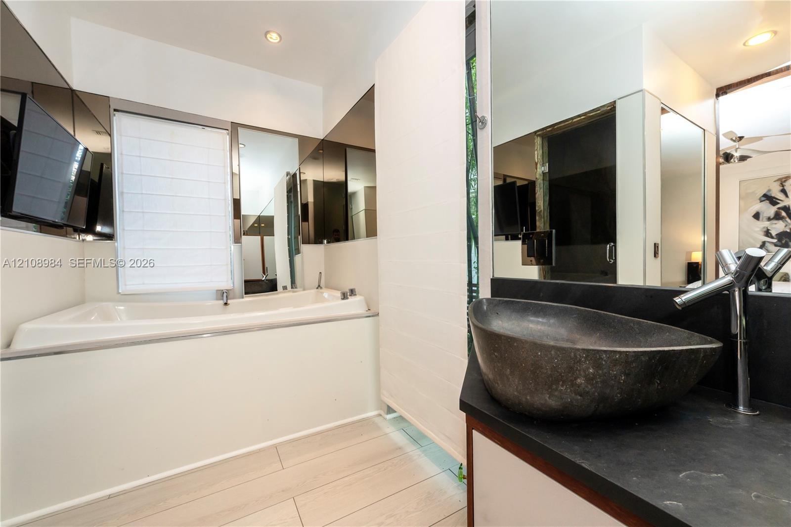 Recessed lighting, deep-basin vessel sink with a contemporary chrome faucet, matte black countertop, mirrored wall accents, and an integrated soaking 